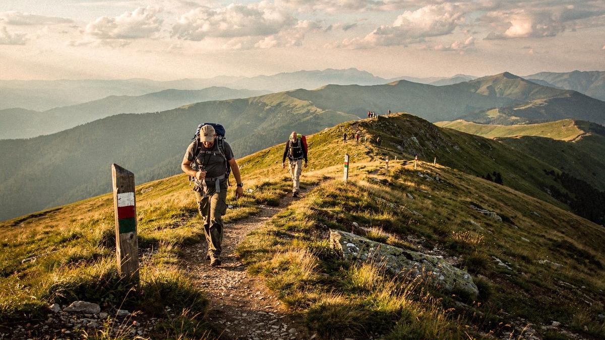 Walkers on a Carpathian ridge path marked with route posts at golden hour